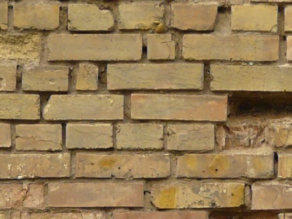 Brick wall texture in mixed colors with very worn, damaged surface and holes.