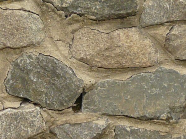 Stone wall containing stones of mixed shapes and sizes set in brown concrete.