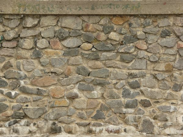 Stone wall containing stones of mixed shapes and sizes set in brown concrete.