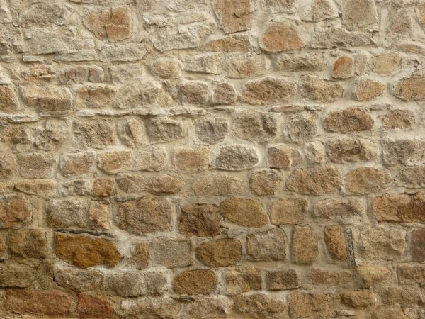 Texture of medieval, stone wall in beige and brown colors set in uneven formation.