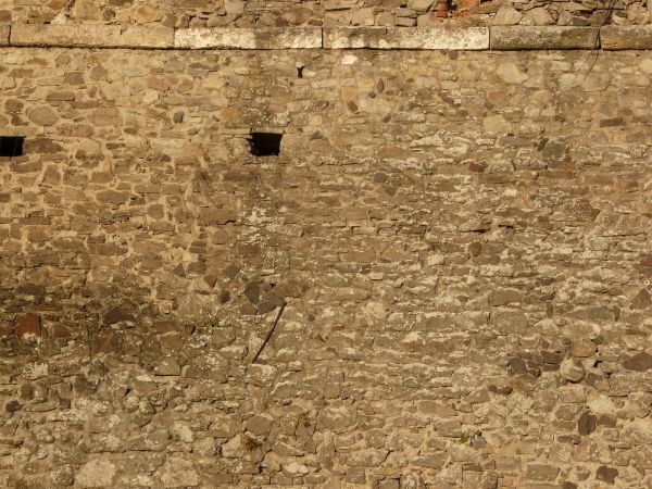 Medieval stone wall texture with holes and worn surface.