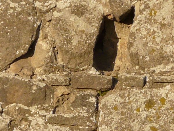 Medieval stone wall texture with holes and worn surface.