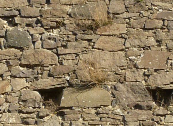 Medieval texture of irregular, stone wall with holes and slightly worn surface.