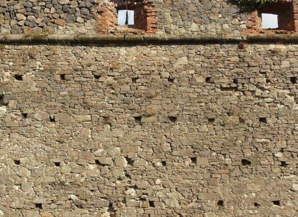 Medieval texture of irregular, stone wall with holes and slightly worn surface.