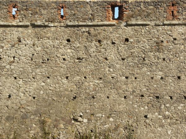 Medieval texture of irregular, stone wall with holes and slightly worn surface.