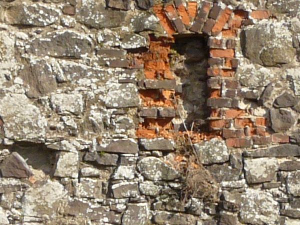 Medieval stone wall with rough texture and windows and holes in surface.