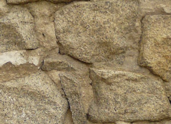 Wall texture made up of red brick and large grey stones. Uneven white cement is visible between many of the bricks, and bright green plants hang down from the top rows.