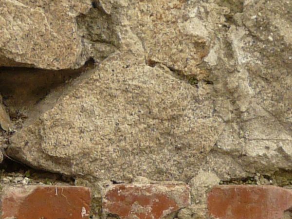 Brick wall texture made up of large grey stones and horizontal rows of red brick. Dark gaps and green moss are visible between many of the bricks.