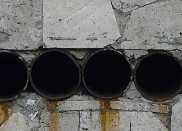 Grey wall texture, made up of bricks of various shapes and sizes. A horizontal row of dark, circular pipe openings runs through the middle of the wall.