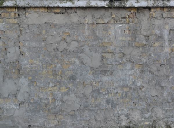 Tan brick wall texture covered almost completely by an rough, uneven layer of dark grey cement.