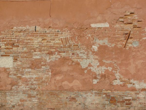 Red wall texture made up of smooth bricks with gaps visible in between, and large areas of erosion and red cement.