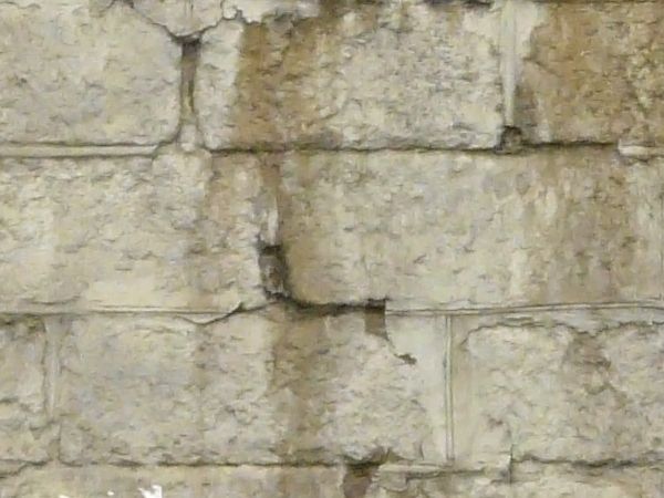 Old brick wall painted white with dark spots across the surface.