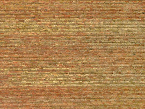 Old brick wall of tan and red tones with holes and spots on surface.