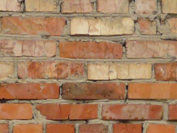 Wall of beige and red bricks set loosely in grey cement with large spots and holes.