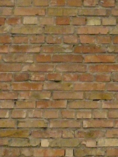 Rustic brick wall of tones of red and beige with stains and holes.