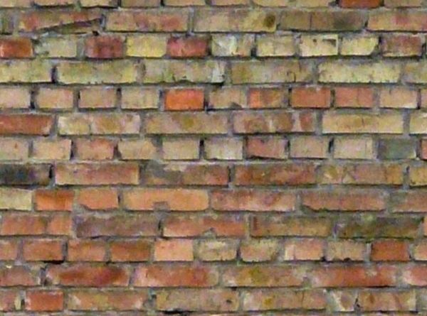 Rustic brick wall of tones of red and beige with stains and holes.