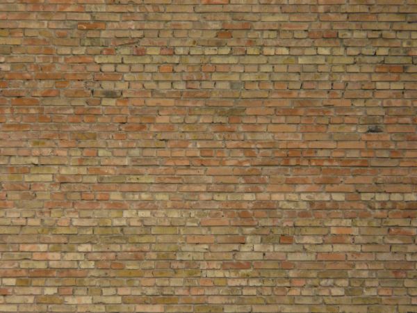 Rustic brick wall of tones of red and beige with stains and holes.