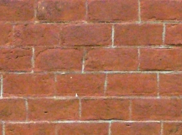 Brick wall in dark red tone with dark spots and light grey cement.