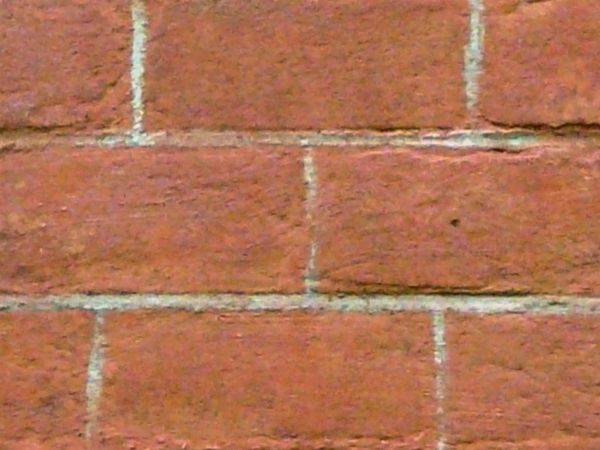 Brick wall in dark red tone with dark spots and light grey cement.