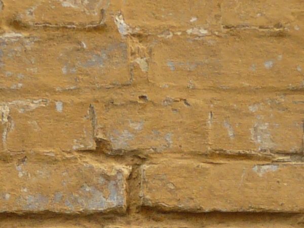 Dirty brick wall painted in light brown color with spots and scratches on surface.