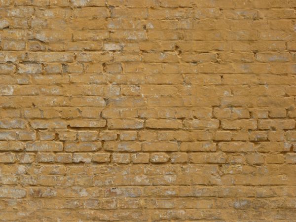 Dirty brick wall painted in light brown color with spots and scratches on surface.