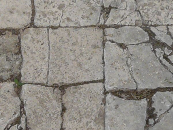 Pavement texture consisting of cracked, rectangular tiles in grey color.