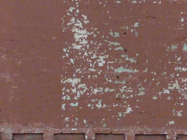 Texture of two-storey building with brick wall painted in red tone. Surface of wall is very worn and dirty.