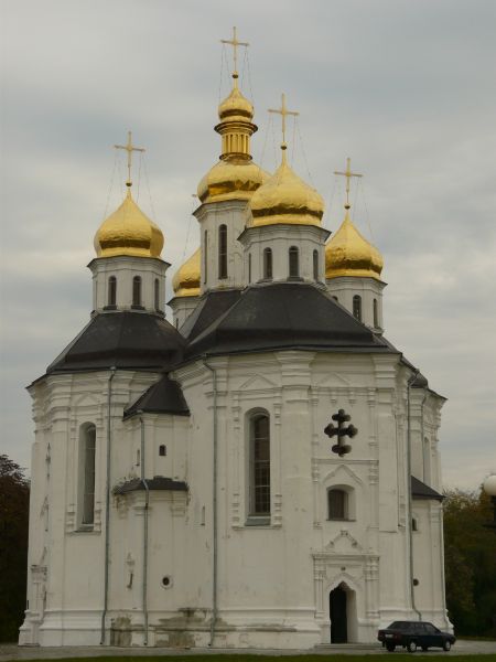 Tall church façade in white and grey with gold-coated domes and crosses on top of tall steeples.