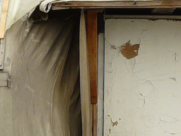 Very small, old shed covered in grey, plastic tarp with wooden door and metal chimney.
