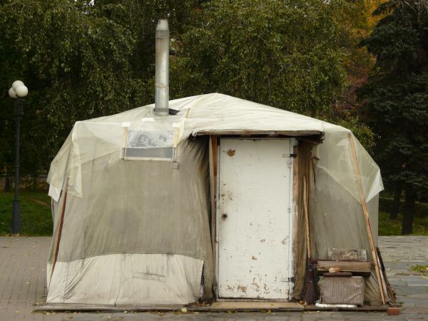Very small, old shed covered in grey, plastic tarp with wooden door and metal chimney.