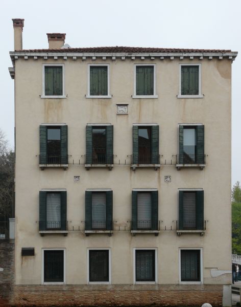 Simple, aged multi-storey building with very worn, beige surface and square windows.