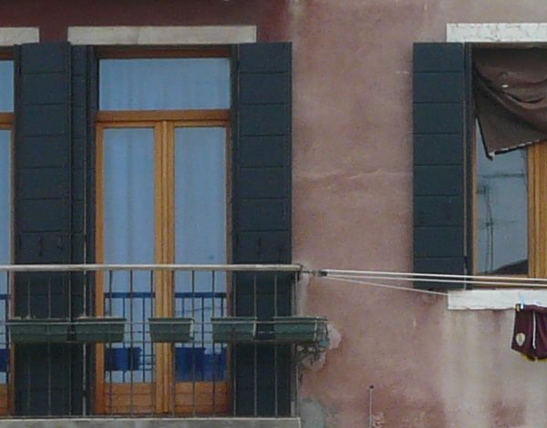 Very old building with worn, concrete walls in pink tone and old windows and balconies on front.