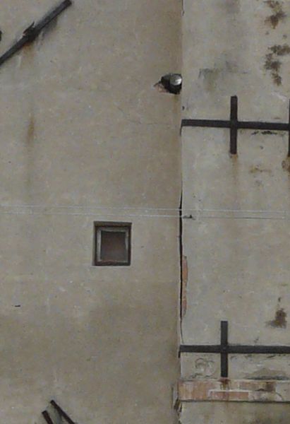 Old, tall building with very irregular, worn surface. A single, stone chimney is attached to front of building.