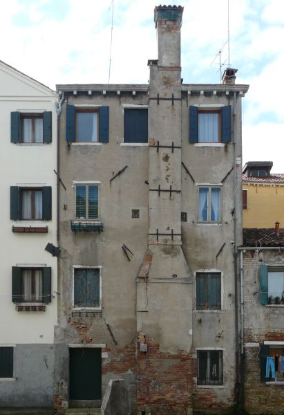 Old, tall building with very irregular, worn surface. A single, stone chimney is attached to front of building.
