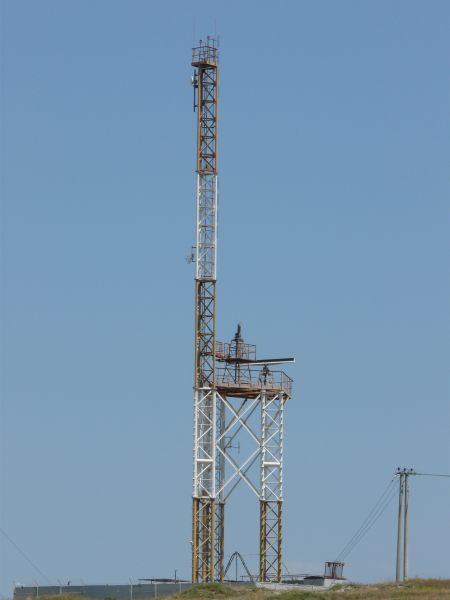 White and brown tower texture, made up of a lattice of painted steel bars. Various attenae and small dishes are attached throughout.