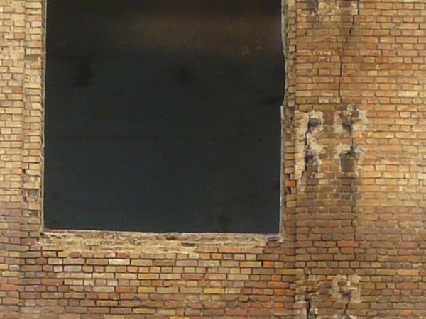 Large, abandoned building of brick with very worn, stained surface.