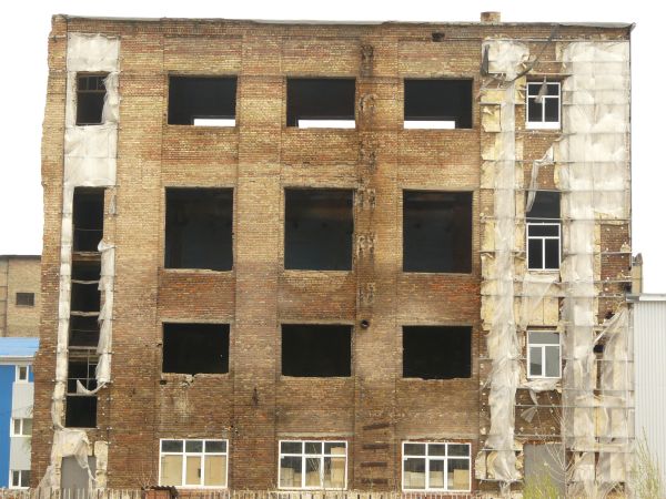Large, abandoned building of brick with very worn, stained surface.