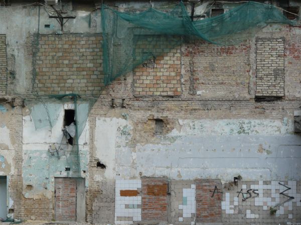 Old, large wall texture of brick and worn concrete with very damaged, irregular surface and hanging nets.