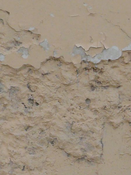 Old wall texture of worn brick and thin layer of concrete painted over in light beige tone.