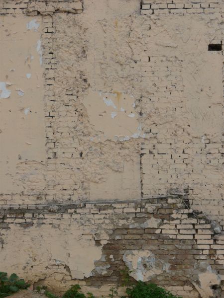 Old wall texture of worn brick and thin layer of concrete painted over in light beige tone.