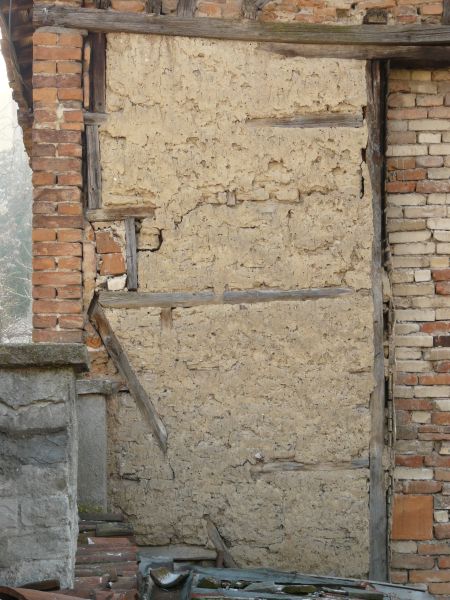 Old brick wall with wooden frame and thin layer of rough concrete with uneven, cracked surface.
