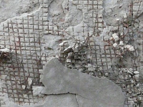 Very damaged concrete surface with exposed metal mesh and rust armature.