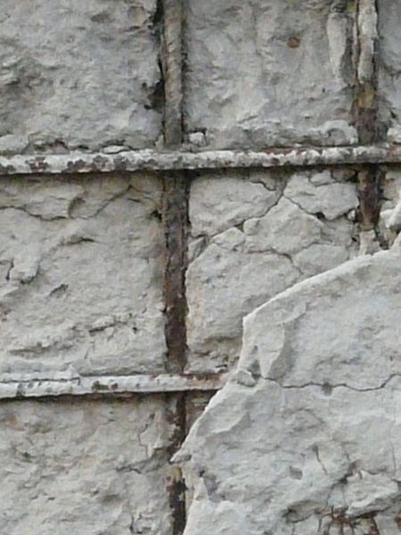 Very damaged concrete surface with exposed metal mesh and rust armature.