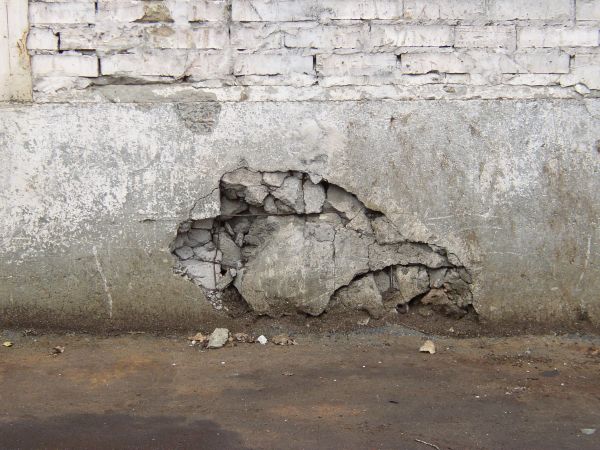 Wall base made of grey concrete with very worn surface and large hole in center.