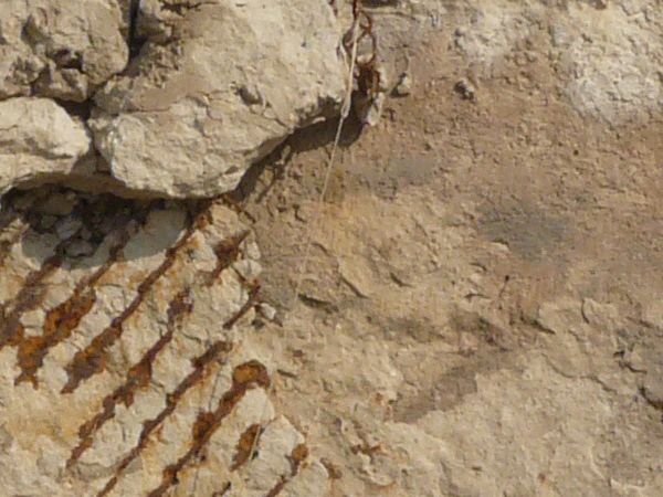 Very rough, damaged concrete in light beige color settled over rusty, metal mesh.