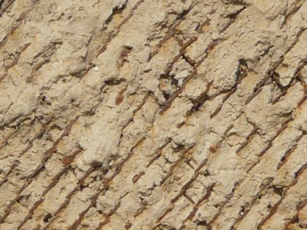 Very rough, damaged concrete in light beige color settled over rusty, metal mesh.