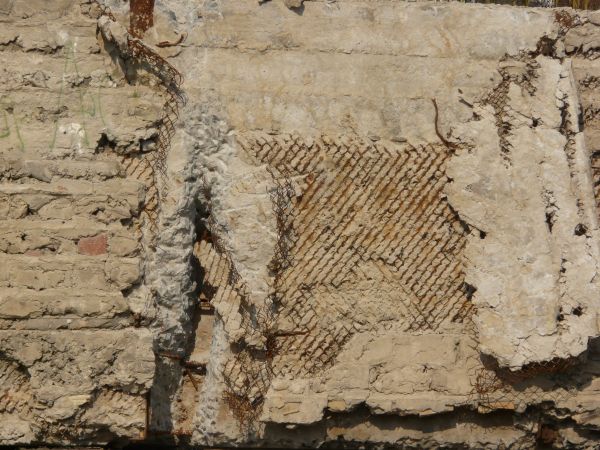 Very rough, damaged concrete in light beige color settled over rusty, metal mesh.