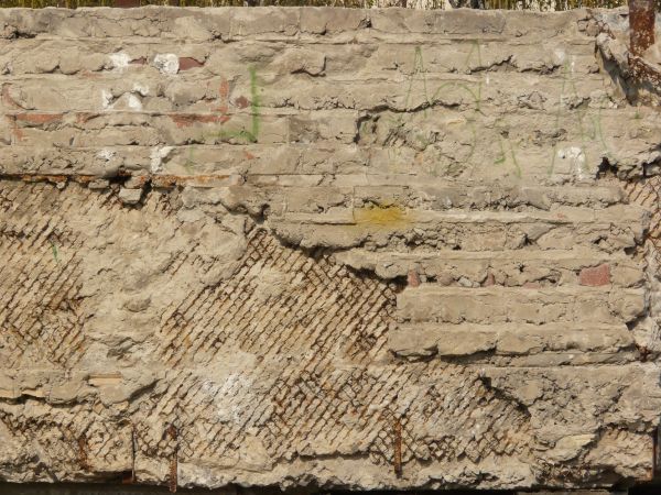 Very rough, damaged concrete in light beige color settled over rusty, metal mesh.