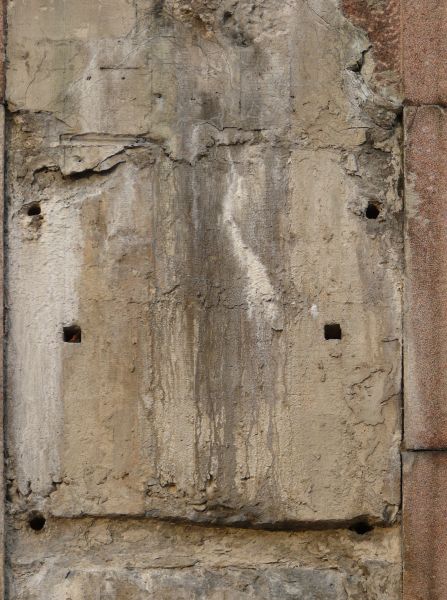 Concrete texture in light brown tone with very rough, irregular surface and dark, vertical streaks.