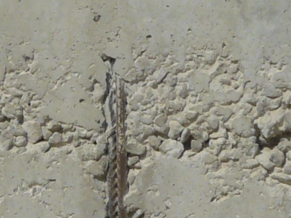 Concrete wall with metal stakes and smooth surface. Concrete is chipped in areas near metal stakes.
